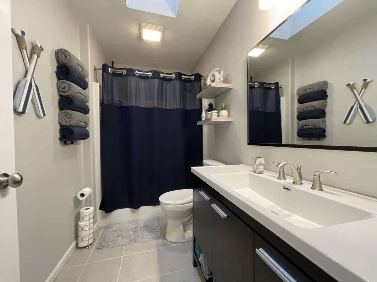 A modern bathroom with a large mirror, two sinks, a toilet, and a shower curtain.