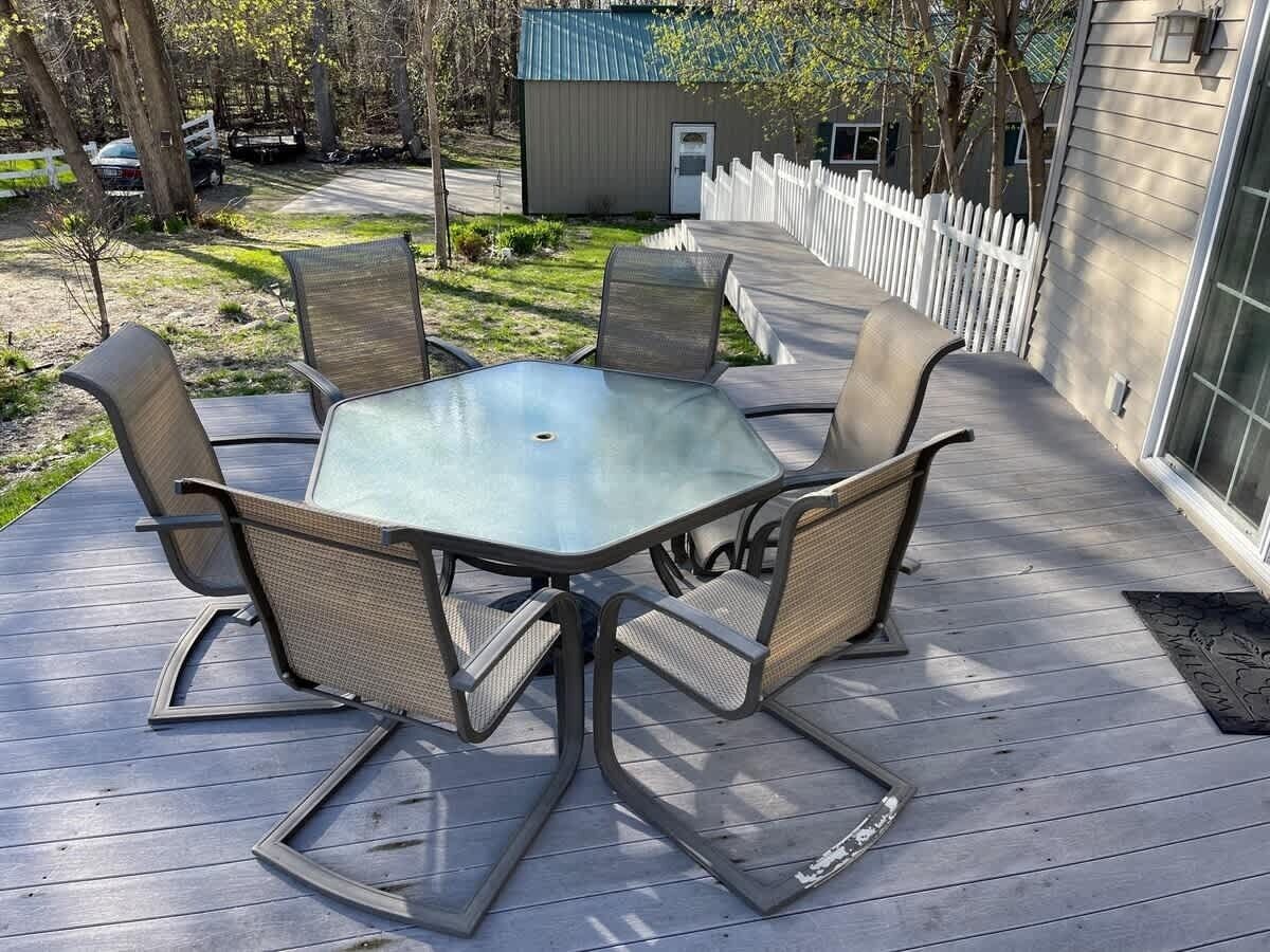 Eine Terrasse mit einem Tisch mit Glasplatte und vier Stühlen, umgeben von einem weißen Zaun aus Holzlatten.
