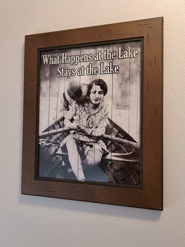 A framed photograph with text 'What Happens at the Lake Stays at the Lake' and a vintage photo of a woman in a boat.