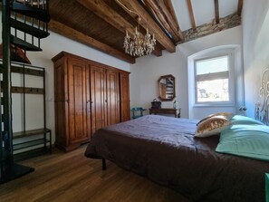 A bedroom with a large bed, wooden wardrobe, a chandelier, and a window with a view.