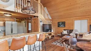 A spacious living area with a wooden staircase, a kitchen with stainless steel appliances, and a bar area with stools.