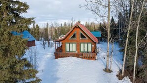 A cabin with a red roof, surrounded by snow-covered ground and trees.