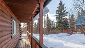 A wooden cabin with a covered porch and a view of a snowy landscape.
