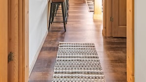 A wooden interior hallway with a patterned rug, a dining area with stools, and a door leading to another room. - Dreamy 2 Bed Cabin #2 - Alaska Kenai Getaway (Sterling)