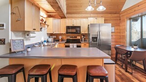 A modern kitchen with wooden cabinetry, stainless steel appliances, and a central island with bar stools. - Dreamy 2 Bed Cabin #2 - Alaska Kenai Getaway (Sterling)