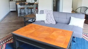 A spacious living area with a wooden ceiling, a blue patterned rug, a sofa, and a coffee table. - Binnekill Views- Cozy Apt over looking the Binnekill stream (Margaretville)