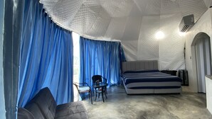 A room with a bed, a chair, a table, and a window with blue curtains. - Dome tent in beautiful countryside, 20 minutes from the beach (Santa Marta de Hojancha)