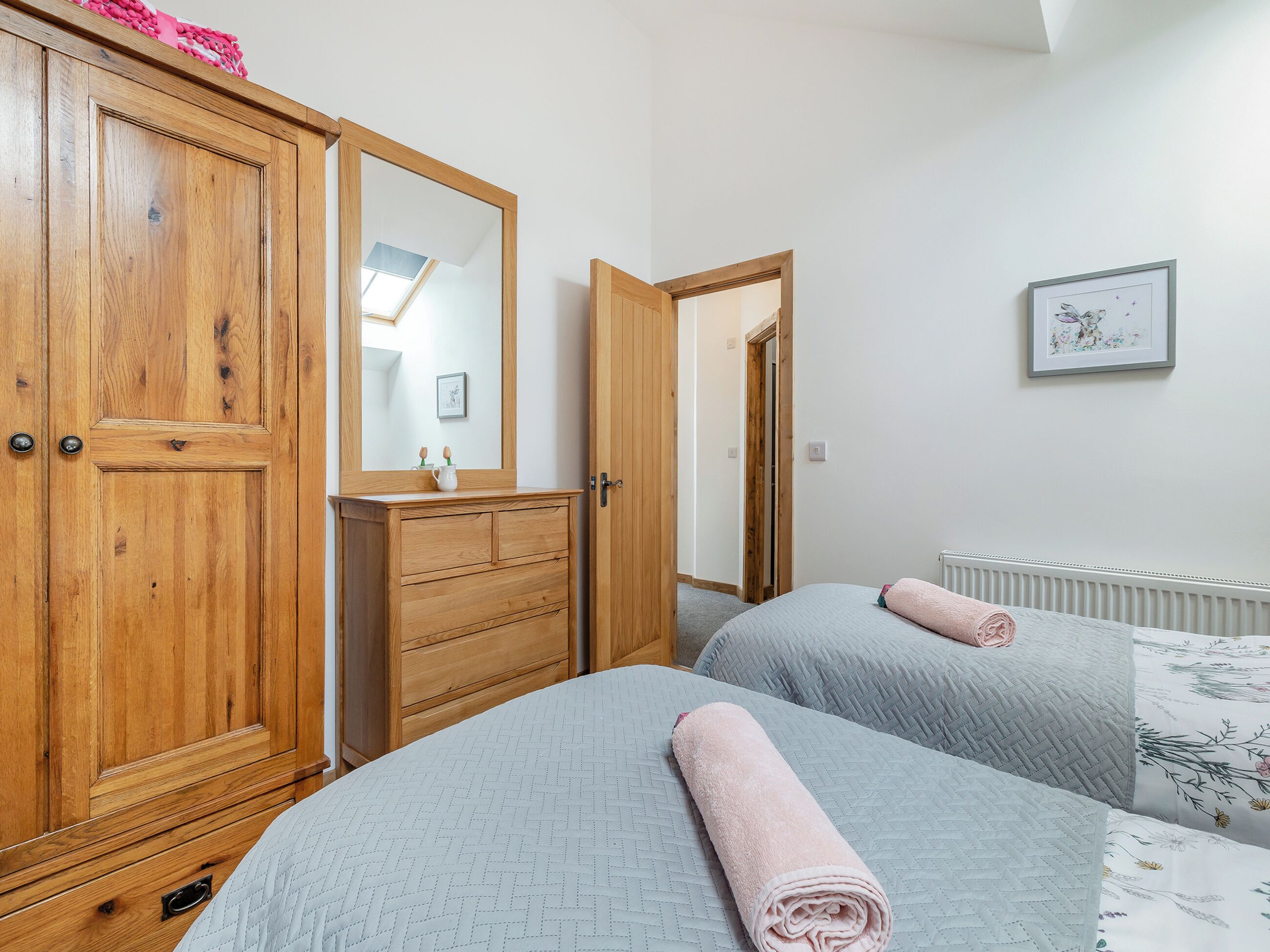 A bedroom with two beds, a wooden wardrobe, a mirror, and a radiator.