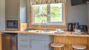 A compact kitchen with a microwave, stove, sink, and bar stools.