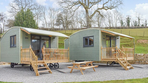 Two small, single-story mobile homes with wooden railings and steps, each with a small porch and a window.