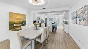 A modern kitchen with white cabinets, a central island, and a dining area with a table and chairs.