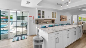 A modern kitchen with white cabinets, a marble countertop, and a view of a pool.
