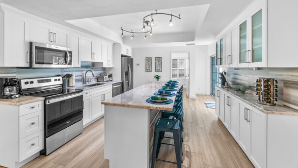 A modern kitchen with white cabinetry, stainless steel appliances, and a central island with bar stools.