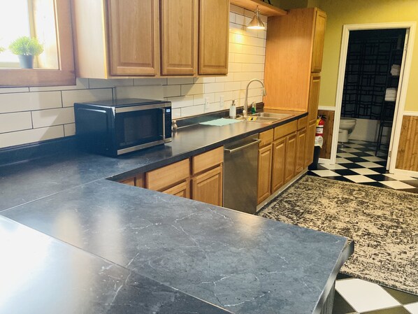 A kitchen with wooden cabinets, a black countertop, a microwave, a sink, and a checkered floor.