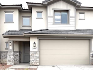 A two-story residential building with a garage, stone foundation, and a 'Welcome' sign.