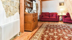 Un salon chaleureux avec un mur en pierre, des meubles en bois, un canapé rouge et un tapis à motifs.