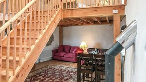 Un escalier en bois menant à un niveau supérieur, un coin repas avec une table et des chaises, et un canapé rouge.