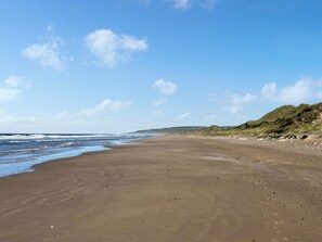 A wide sandy beach with gentle waves, a clear sky, and grassy dunes in the distance. - Ballygroggan Bungalow - UK38174 (Machrihanish, near Campbeltown)