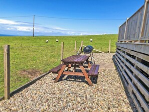 A picnic area with a grill, wooden table, and benches, surrounded by a fence and a grassy field with sheep. - Ballygroggan Bungalow - UK38174 (Machrihanish, near Campbeltown)