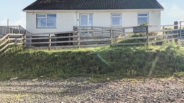 Une maison de plain-pied avec un toit en tuiles, une clôture en bois et une allée gravillonnée.