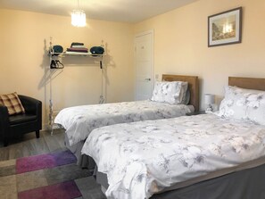 A bedroom with two beds, a chair, a lamp, a shelf with folded clothes, and a door. - Ballygroggan Bungalow - UK38174 (Machrihanish, near Campbeltown)