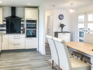 Une cuisine moderne dotée d’appareils électroménagers intégrés, un coin repas avec une table et des chaises en bois, et une horloge murale décorative.