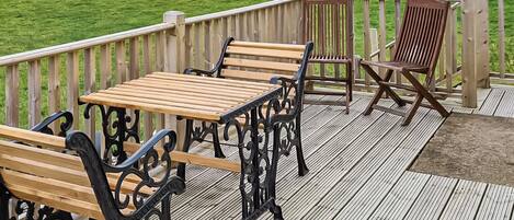Une terrasse en bois, agréée de mobilier d’extérieur, notamment des bancs et une table, donnant sur une zone herbeuse et offrant une vue sur l’eau.