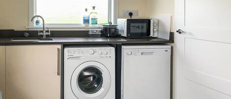 A compact laundry area with a washing machine, dryer, microwave, and sink.