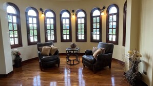 Una habitación con techo curvo, suelo de madera y seis ventanas arqueadas con iluminación. Hay dos sillones de cuero y una mesita con un objeto decorativo.