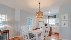 Une cuisine moderne avec des meubles blancs, une table à manger avec des chaises et un luminaire suspendu.