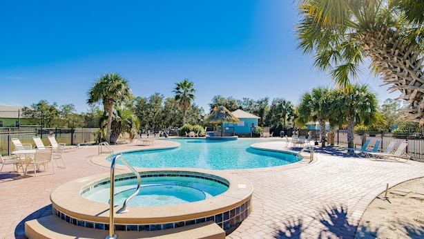Une piscine avec un jacuzzi, entourée de chaises longues et de palmiers.