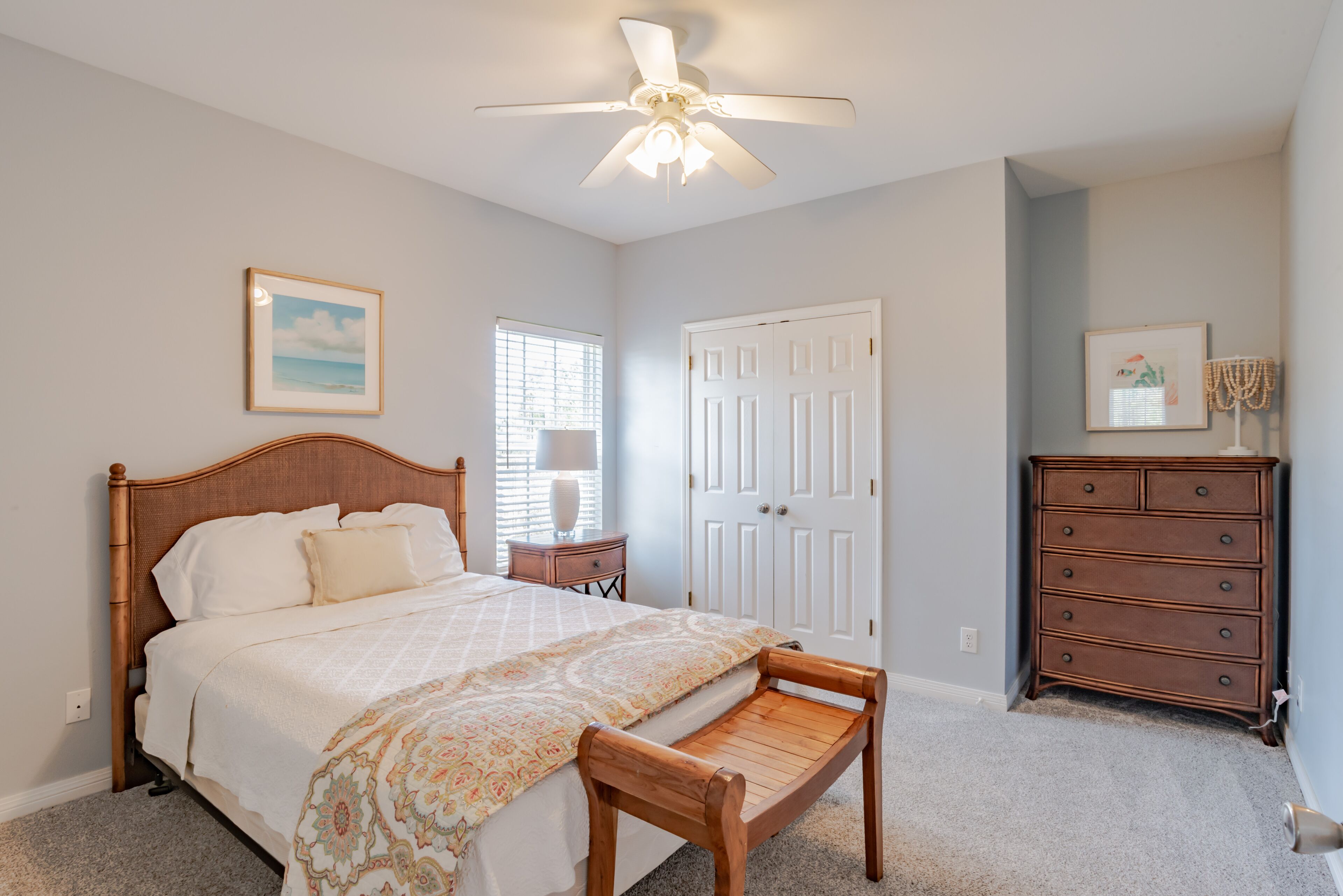 A bedroom with a bed, a wooden bench, a dresser, and a ceiling fan.