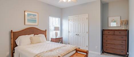A bedroom with a bed, a wooden bench, a dresser, and a ceiling fan.