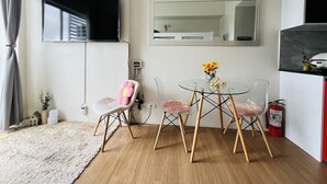 A modern living room with a glass table, two chairs, a TV, a clock, and a mirror on the wall. - Bright Studio Sleeps 3 With Parking and City View (Cagayan de Oro)