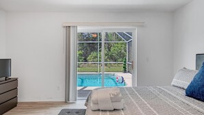 A bedroom with a large bed, a TV, and a view of a swimming pool through a sliding glass door. - **EXCLUSIVE 3-bedroom w/heated private pool** (Palm Coast)