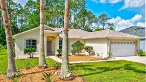 A single-story house with a garage, surrounded by a well-maintained lawn and several trees. - **EXCLUSIVE 3-bedroom w/heated private pool** (Palm Coast)