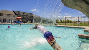 Una piscina con fuente acuática, rodeada por una valla y edificios al fondo.