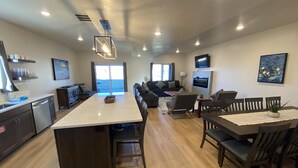 Una cocina moderna con una isla central, comedor con sillas de madera, un sofá y un televisor en la pared.