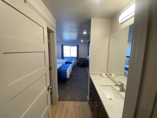Ein Hotelzimmer mit einem großen Bett, einer separaten Sitzecke, einem Badezimmer mit einem großen Spiegel und Blick ins Freie durch ein Fenster.