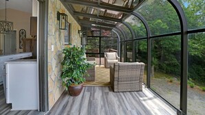 A glass-enclosed patio with wicker furniture, a potted plant, and a view of the surrounding forest. - Ridge View - Hot Tub-Fireplace-Fire Pit (Hiawassee)