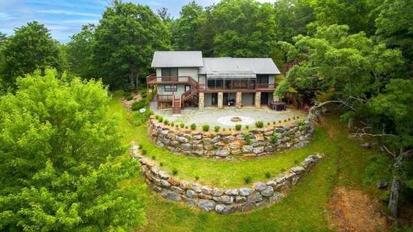 A two-story house with a stone retaining wall, a deck, and a fire pit.