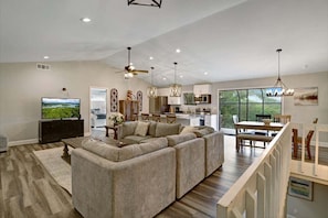 A spacious living room with a sectional sofa, a flat-screen TV, and a dining area with a table and chairs.