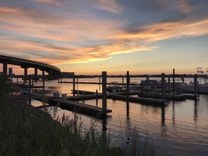 Un puerto deportivo con barcos amarrados, un puente al fondo y un cielo al atardecer.