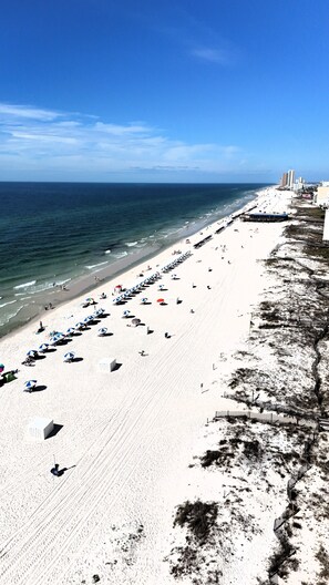 A beach with umbrellas and sun loungers, a pier, and buildings in the background.