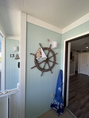 Una habitación con decoración náutica en la pared, un cartel con el número '13' y una chaqueta azul colgada en la puerta.