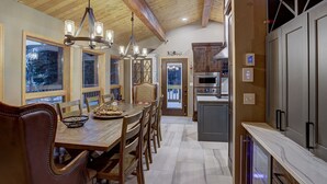 Una cocina amplia con armarios de madera, un comedor con una gran mesa y sillas de madera, y vistas al exterior a través de amplios ventanales.