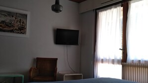 Une pièce comprenant un lit, une chaise, une petite table, un téléviseur à écran plat et un tableau accroché au mur.