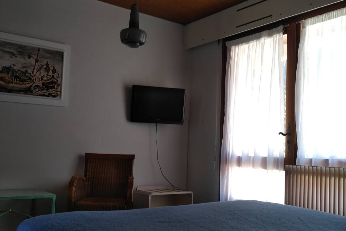 Une pièce comprenant un lit, une chaise, une petite table, un téléviseur à écran plat et un tableau accroché au mur.
