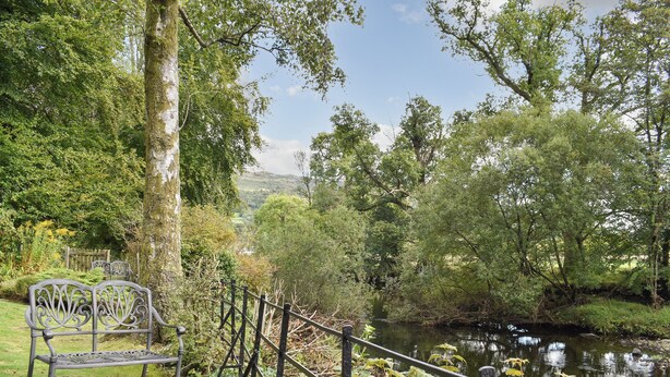 A bench and a fence by a calm river with trees in the background.