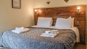 A hotel room with a wooden headboard, two wall-mounted light fixtures, a framed certificate on the wall, and a neatly made bed with towels.